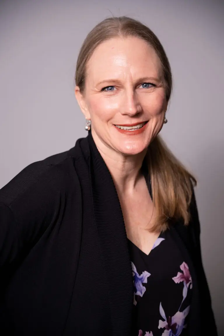 Head and shoulders photos of Heather, white woman with long blonde hair in a ponytail. She is wearing a flowered blouse and dress jacket and smiling.